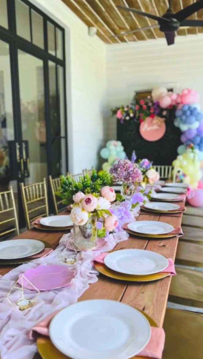 Outdoor farmhouse table baby shower with pink runner peonies gold chargers and rainbow balloon arch at Carissa Venue